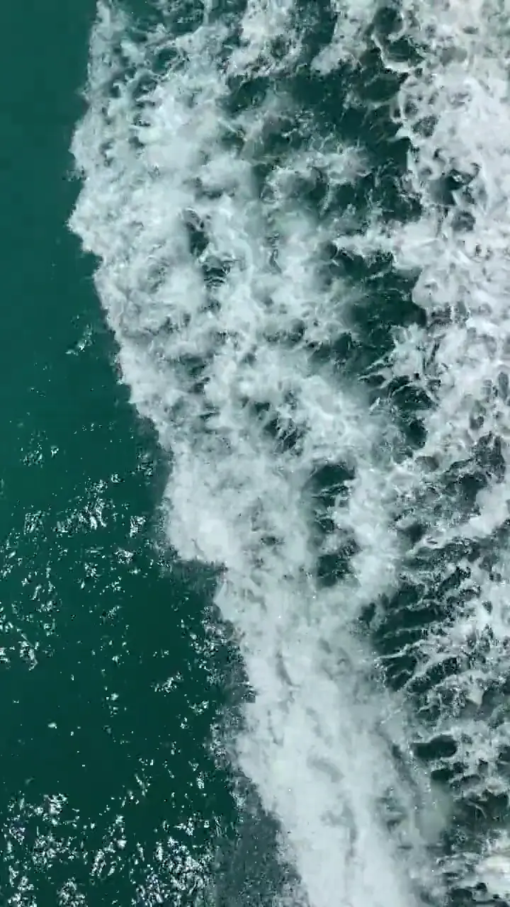 Vertical aerial view of turquoise ocean waves rolling ashore